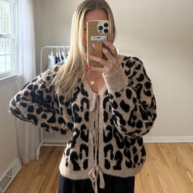 Person wearing a leopard print sweater taking a mirror selfie in a room with a window and wooden floor.