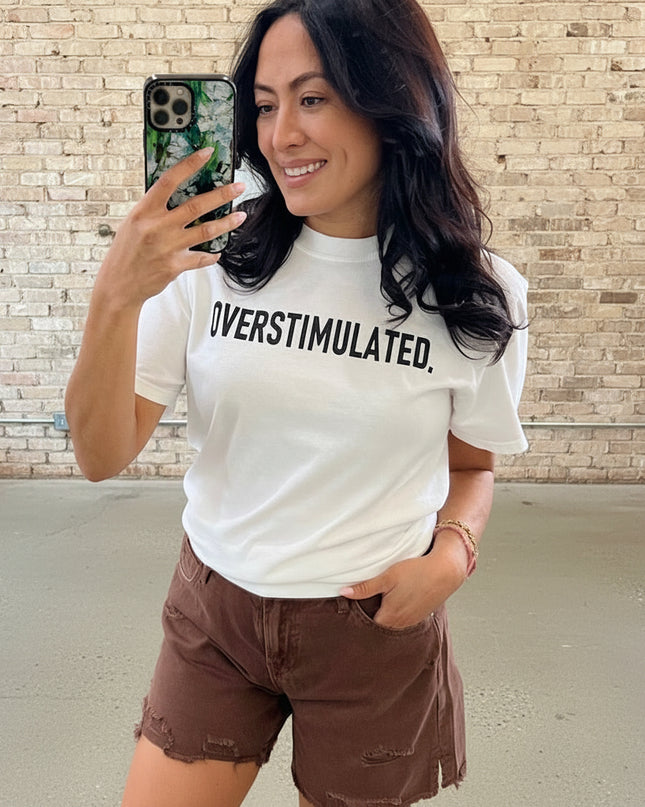 Woman wearing a white t-shirt with 'OVERSTIMULATED' text in a store setting.
