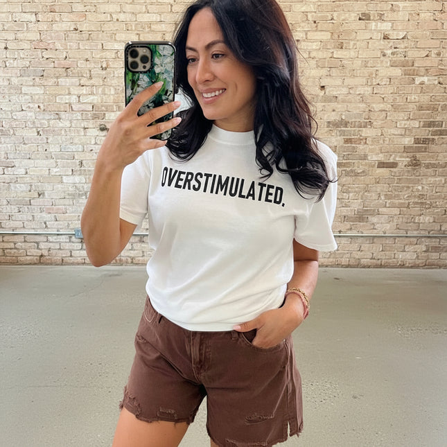 Woman wearing a white t-shirt with 'OVERSTIMULATED' text in a store setting.